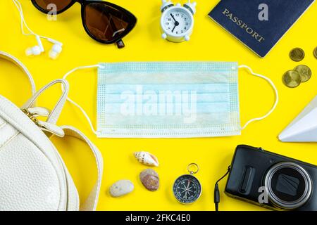 Reisepass, medizinische Maske und Sonnenbrille auf gelbem Hintergrund. Sicheres Reisekonzept während der Coronavirus-Pandemie. Flatlay, Kopierbereich. Stockfoto