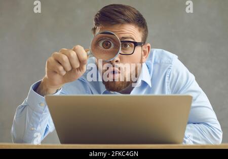 Lustig überrascht Geschäftsmann mit Laptop Blick auf etwas durch Vergrößerungsglas Glas Stockfoto
