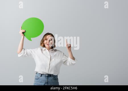Glückliche übergewichtige Frau in weißem Hemd mit grüner Sprechblase Und zeigt mit Finger isoliert auf grau Stockfoto