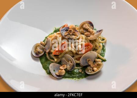 Vollkornpasta mit Meeresfrüchten, große hausgemachte Spaghetti mit Muscheln, Kirschtomaten, Haselnüssen und Pesto, Nahaufnahme von withem Gericht Stockfoto