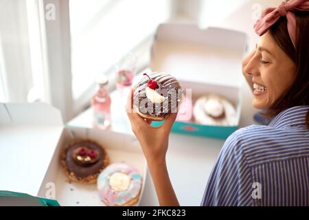 Ein schönes Mädchen in einer angenehmen Atmosphäre in einer Konditorei schaut leidenschaftlich auf einen leckeren Donut, den sie kaum wartet versuchen. Konditorei, Dessert, sw Stockfoto