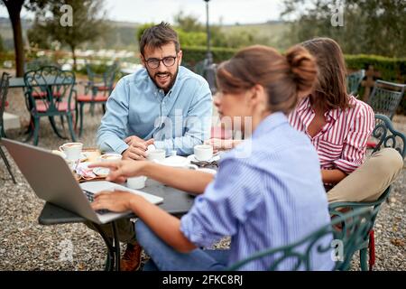 Gruppe von Studenten, die zusammen Papier schreiben, während sie draußen Kaffee trinken Stockfoto