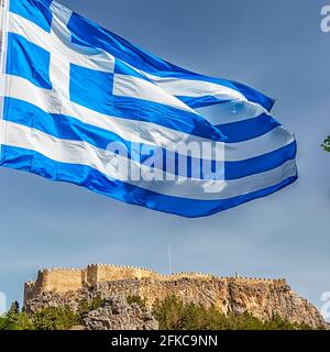 Die griechische Flagge schwingt über den Mauern, die den Tempelkomplex umgeben, der die Akropolis von Lindos auf der griechischen Insel Rhodos ist. Stockfoto