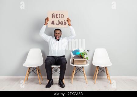 In voller Länge Körpergröße Foto von wütenden Mann sitzen warten Für Interviews schreiend brauchen Job Geld zeigen Pappe Stockfoto