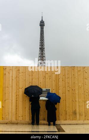 Menschen mit Schirmen, die durch die Baustelle schauen, sichern sich ein Fencing-Fenster mit dem Eiffelturm im Hintergrund, Paris, 2014. Stockfoto