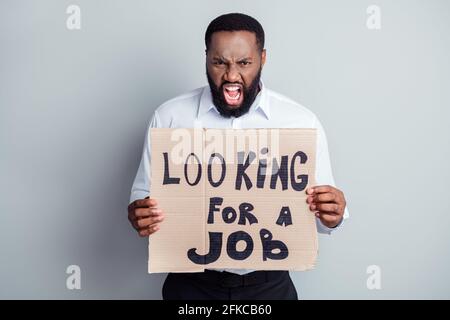 Fotoporträt eines wütenden wütenden Mannes, der Pappe bei verlorener Arbeit hält Job muss auf grauem Hintergrund isoliert werden Stockfoto