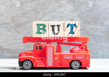 Roter Feuerwehrwagen hält Buchstabenblock in Wort, aber an Holzhintergrund Stockfoto