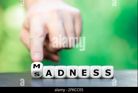 Wahnsinn oder Traurigkeit? Die Hand dreht Würfel und ändert das Wort „Adness“ in „Adness“. Stockfoto