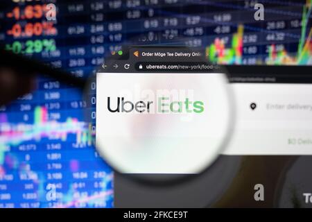 Uber frisst Firmenlogo auf einer Website mit verschwommenen Börsenentwicklungen im Hintergrund, die durch eine Lupe auf einem Computerbildschirm zu sehen sind Stockfoto
