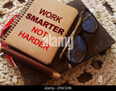 Stift, Brille und Spiralheft mit Work Smarter nicht härtere Wörter auf gehäkelter Stoffhintergrund. Karriere- und Geschäftskonzept Stockfoto