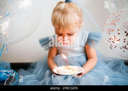 Das kleine blonde Mädchen bläst die Kerzen auf dem Geburtstagskuchen aus. Stockfoto