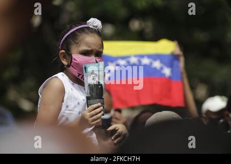 Caracas, Venezuela. April 2021. Ein Mädchen, das von Mund zu Nase bedeckt ist und auf den Schultern eines Erwachsenen sitzt, hält ein Bild des venezolanischen Arztes Jose Gregorio Hernandez vor der Kirche hoch, in der Hernandez selig gesprochen wird. Hernandez wird in Venezuela als der "Doktor der Armen" verehrt. Kredit: Jesus Vargas/dpa - ACHTUNG: Nur für redaktionellen Gebrauch und nur mit vollständiger Erwähnung des oben genannten credit/dpa/Alamy Live News Stockfoto