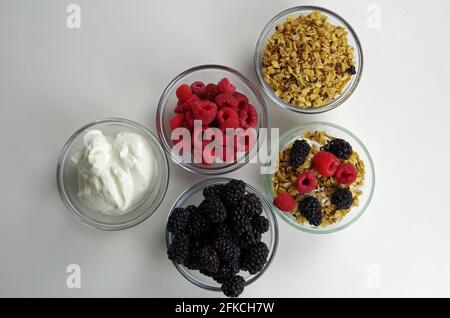 Gesunde Zutaten für die Zubereitung von Snacks oder Mahlzeiten, darunter Joghurt, Himbeeren, Brombeeren und Müsli Stockfoto