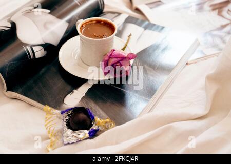 Selektive Fokus EIN türkischer Kaffeebecher und eine getrocknete Rose auf dem Teller davon . Einige öffnen Zeitschriften darunter und eine Schokolade bereit zu beißen. Stockfoto