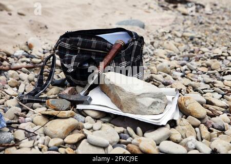 Geologen Beutel mit den Steinen und Notizen Papiere und Hammer. Konzept der Geologie-Wissenschaft. Der Hammer und das Mineral des Geologen sind auf einem Kiesel angelegt Stockfoto