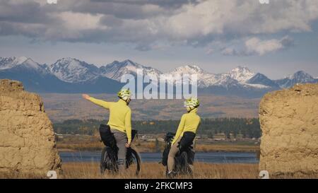 Der Mann und die Frau reisen auf gemischtem Terrain mit Bikepacking. Die beiden Personen reisen mit Fahrradtaschen. Schneebedeckte Berge, Steinbogen. Stockfoto