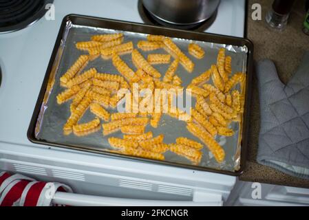 Ein mit Folie ausgekleidete Backblech, bedeckt mit gefrorenen pommes Frites, wartet darauf, in den Ofen zu gehen Stockfoto