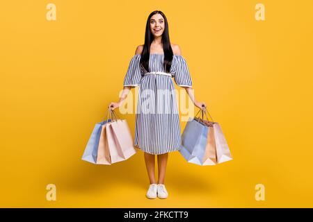 In voller Länge Foto von ziemlich beeindruckt junge Dame tragen gestreift Kleid mit Schnäppchen isoliert gelbe Farbe Hintergrund Stockfoto