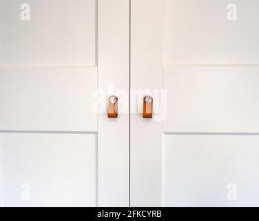 Weiße Schranktüren aus Holz mit braunen Ledergriffen aus Holz Nahaufnahme Hintergrundstruktur des Schranks Stockfoto