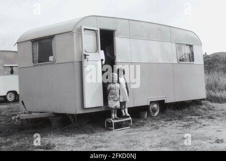 1960er Jahre, historisch, zwei kleine Kinder, ein Bruder und eine Schwester, die auf einem Schritt vor dem Eingang zu einem Urlaub Karawane der Zeit in einem Feld von Sanddünen geparkt, England, Großbritannien. Stockfoto