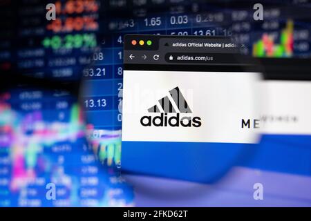 Adidas Firmenlogo auf einer Website mit verschwommenen Börsenentwicklungen im Hintergrund, die auf einem Computerbildschirm durch eine Lupe gesehen werden Stockfoto