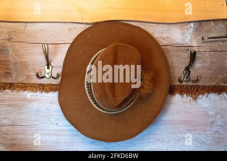 Wandhaken mit einem braunen Hut, der darauf hängt. Wandhaken aus Holz mit Metallhaken. Ein schöner Kuhbogenhut, der an einer braunen Holzwand hängt. Zakopane, Polen. Hochwertige Fotos. Stockfoto