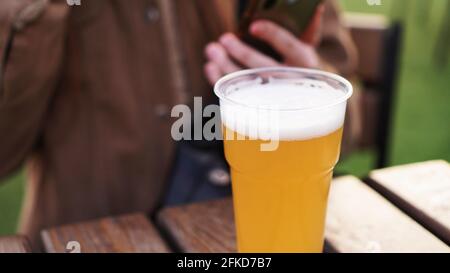 Leichtes Bier in einem Plastikglas. Mädchen trinkt Bier am Food Court - verschwommener Hintergrund Stockfoto