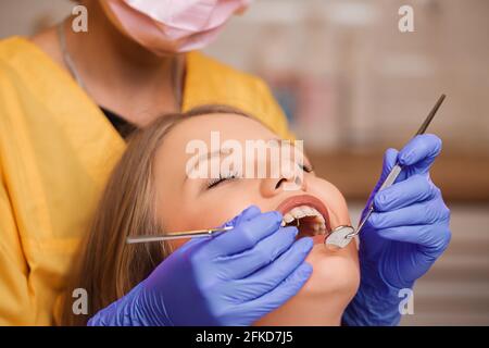 Schöne blonde Patientin beim Zahnarzt. Die jungen Frauenzähne werden von einer Zahnärztin mit Hilfe von speziellen medi untersucht, untersucht und behandelt Stockfoto