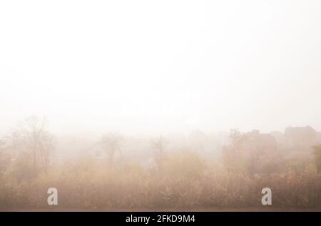 Ein nebliger Morgen in einer Dorflandschaft. Landhäuser in Nebelansicht. Friedliche Bäume und kleine ländliche Dorf. Rustikales Hintergrundbild. Stockfoto