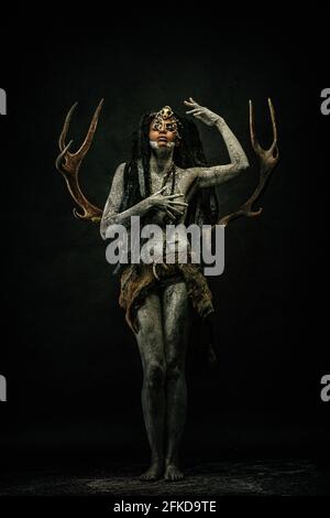 Stammesschamane mit Lehm bedeckt, Dreadlocks, Knochenketten und Hirschgeweih auf dem Rücken tragend Stockfoto