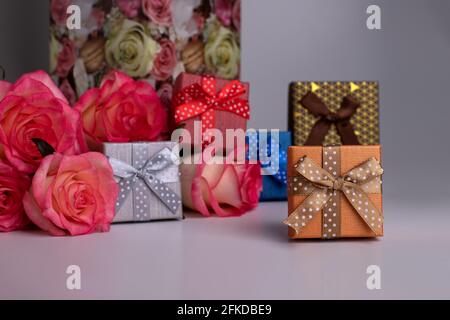 Kleine Geschenkschachteln in verschiedenen Farben und ein Strauß rosa Rosen. Schmuckkisten. Auf dem Tisch stehen rosa Rosen. Blumenstrauß. Stockfoto