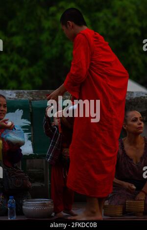 Luang Prabang, Laos - 6. Juli 2016: Ein junger buddhistischer Mönch nimmt Reis an, der ihm von einem Kind während der Almosenzeremonie von Sai B am frühen Morgen gegeben wurde Stockfoto