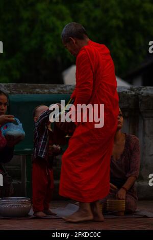 Luang Prabang, Laos - 6. Juli 2016: Ein buddhistischer Mönch nimmt Reis an, der ihm von einem Kind während der Almosenzeremonie von Sai bat am frühen Morgen gegeben wurde. Stockfoto