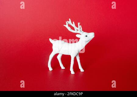 Weisse festliche Rentiere auf rotem Hintergrund. Dekoration Hirsch Spielzeug. Minimalkonzept Weihnachten, Vorderansicht Stockfoto