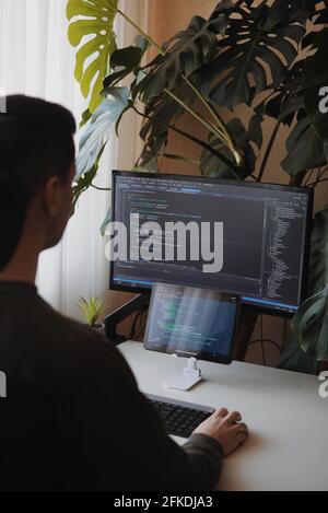 Junge Entwickler arbeitet von zu Hause aus. Programmiergerät codiert mit Bildschirm und Tablet Stockfoto
