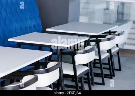 Schwarz-weiße Stühle und Tische auf einem Food Court gegen eine blaue Wand. Café-Innenausstattung. Hochwertige Fotos Stockfoto