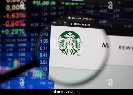 Starbucks Firmenlogo auf einer Website mit verschwommenen Börsenentwicklungen im Hintergrund, die auf einem Computerbildschirm durch eine Lupe gesehen werden Stockfoto