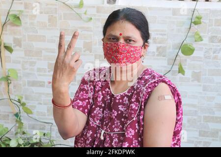 Indische Frau macht Siegeszeichen nach der Impfung während des neuen Covid-19-Stammes erhielt die reife Frau, die eine Maske mit Verband trug, eine Corona Stockfoto