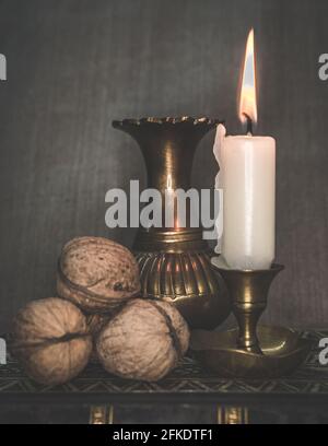 Vertikale Aufnahme von Lichtkerze, Bronzevase und Walnüssen auf einem Tisch Stockfoto