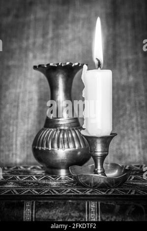 In Graustufen angezündete Kerze mit einer bronzenen Vase Einen Tisch Stockfoto