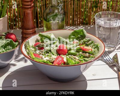 Frische Erdbeeren, grüner Spargel, Feta-Käse, Babyspinat und Rukula-Salat in einer Schüssel mit Mineralwasser serviert. Stockfoto