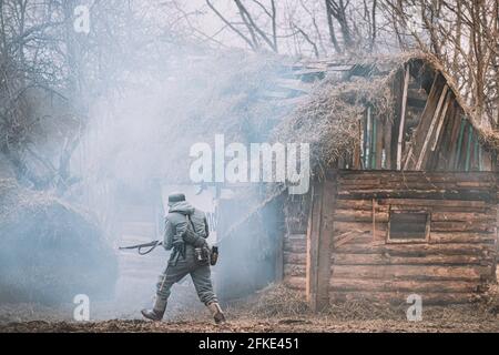 Deutscher Wehrmachts-Infanteriesoldat im 2. Weltkrieg auf dem Schlachtfeld in der Nähe des brennenden Holzhauses. Deutscher Soldat im Zweiten Weltkrieg Warme Herbstkleidung Stockfoto