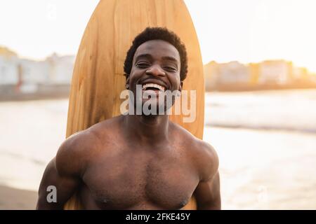 Fröhlicher Afro-Surfer, der Spaß beim Surfen während der Sonnenuntergangszeit hat - Afrikanischer Mann am Tag der Brandung - Extremsport Lifestyle Menschen Konzept Stockfoto