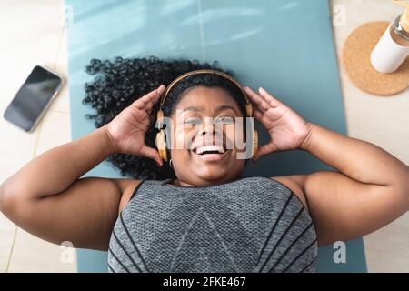 Glückliche afrikanische Frau, die Spaß hat, Musik mit Kopfhörern zu hören, während Pilates zu Hause Stockfoto