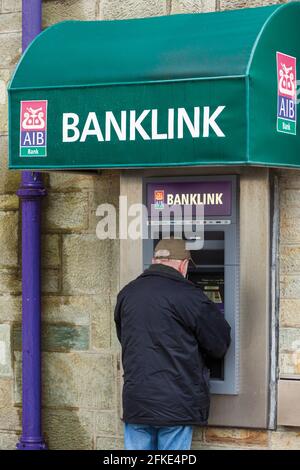 Mann, der einen Geldautomaten oder Geldautomaten, manchmal auch als „Loch in der Wand“ oder Geldautomat in einer Filiale der AIB oder der alliierten irischen Banken bezeichnet, Stockfoto