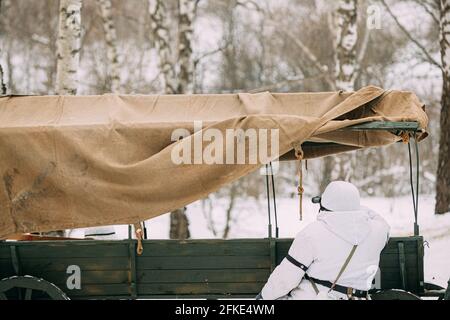 Hidden Re-enactor als deutscher Wehrmachts-Infanteriesoldat in World gekleidet Krieg II Soldaten sitzen in Hinterhalt in der Nähe von Bauernwagen in Winterwald Und Stockfoto