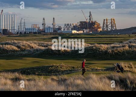 Golfspieler, der im Seaton Carew Golf Club mit dem spielt Das obere Deck der Offshore-Plattform Shell Brent wird demontiert und Recycelt bei able UK in der Ferne Stockfoto