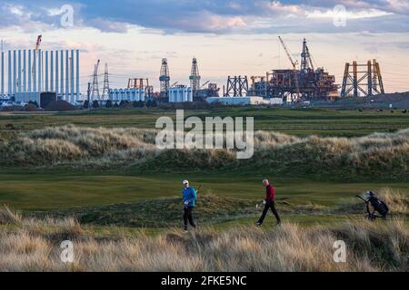 Golfspieler, der im Seaton Carew Golf Club mit dem spielt Das obere Deck der Offshore-Plattform Shell Brent wird demontiert und Recycelt bei able UK in der Ferne Stockfoto