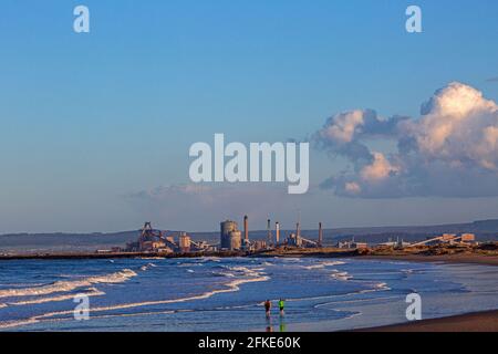 Ein Paar, das am Strand entlang läuft, mit dem Redcar Stahlwerk in der Nähe, England, Großbritannien Stockfoto