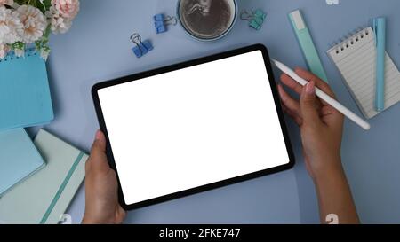 Draufsicht auf die Hand einer Frau, die ein digitales Tablet und einen Stylus-Stift auf einem pastellblauen Hintergrund hält. Stockfoto